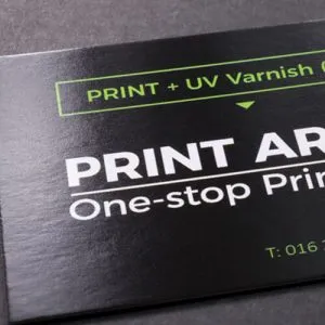 Een close-up van een zwart visitekaartje met een glanzende UV-lakafwerking op de tekst en designelementen.