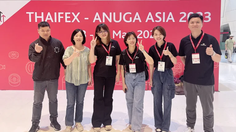El equipo de KanzoPack posando para una foto grupal frente al telón de fondo de la exposición THAIFEX Anuga Asia 2023.